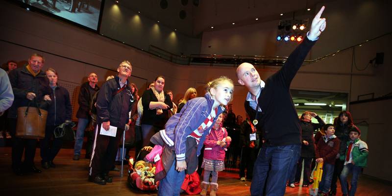 Visitors of all ages to the Royal Concert Hall stand on the stage and are shown around by a member of staff.
